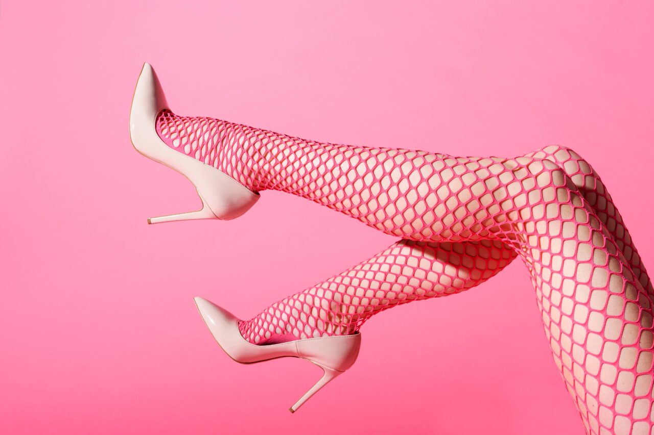 Rosa High Heels und rote Netzstrumpfhose auf pinkem Hintergrund, stilvolles Accessoire für International Escort.